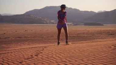 Gezgin, Ürdün çölünün ikonik engebeli dağlarıyla çevrili Wadi Rum 'un kırmızı kumlarında duruyor. Keşif hissi ve uzak manzaraların güzelliği yayıyor.