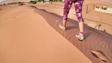 Kadın şafakta Umman 'daki Boş Çeyrek kum tepelerine yavaş çekimde tırmanıyor..