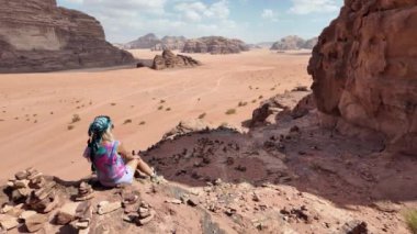Yalnız kız gezgin, Ürdün 'deki Wadi Rum çölünün görkemli manzaralarının arasında oturuyor. Uçsuz bucaksız, kırmızı kumlara ve yükselen kaya oluşumlarına karşı yalnızlığı yansıtıyor.