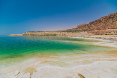 Ürdünlülerin eşsiz doğal güzelliklerini ve Ürdün 'deki mineralzengin manzaralarını gösteren berrak bir gökyüzüne karşı sakin Ölü Deniz manzarası büyüleyici bir manzara.
