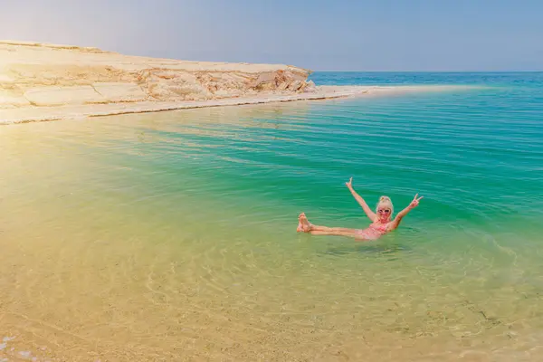 stock image a solitary woman effortlessly floating in the green waters of the Dead Sea making thalassotherapy, surrounded by natural rocky shores in Jordan