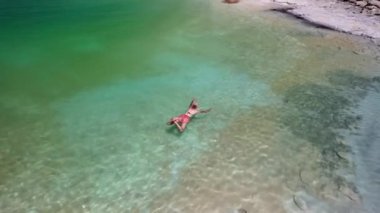 Ölü Deniz 'de dinlenen, talassoterapi yapan, şeffaf ve sığ sularda, Ürdün' de berrak bir gökyüzünün altında, beyaz kumlu bir sahilin yakınında yüzen bir kadının hava manzarası.