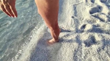 Ürdün 'de, ölü denizin beyaz kumlu sahilinde yürüyen çıplak ayakların yakınlaşması günbatımında dokunulmamış, desenli yüzeyde ayak izleri bırakır.