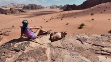 Yalnız kız gezgin, Ürdün 'deki Wadi Rum çölünün görkemli manzaralarının arasında oturuyor. Uçsuz bucaksız, kırmızı kumlara ve yükselen kaya oluşumlarına karşı yalnızlığı yansıtıyor.
