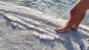 Sakin dalgalar ve berrak suyla Ürdün 'deki Ölü Deniz' in sakin kumlu sahil şeridi boyunca yalın ayak yürümek. Huzurlu deniz kenarı doğası arasında rahatlık ve sükunet sağlıyorum.