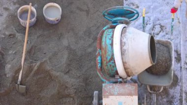 İnşaat alanındaki bir el arabasına beton döken çimento karıştırıcısı. Kovalar, kürek ve görünür bir inşaat işçisi.