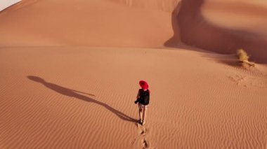 Kum tepelerinde yürüyen bir turist kız arkasında kırmızı kumda ayak izlerini bırakıyor. Umman Çölü 'nü keşfeden, ayaklarının altındaki kumu hisseden Rub al-Khali kumullarının yalnızlığını kucaklayan