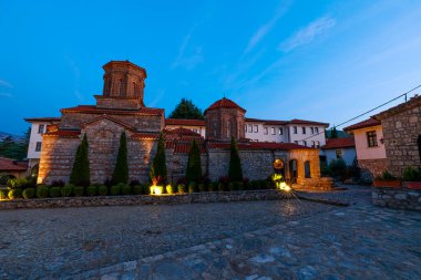 Kuzey Makedonya 'da Ohri Gölü boyunca uzanan renkli alacakaranlık gökyüzünün altındaki Saint Naum manastırının kaldırım taşı avlusu ve aydınlatılmış ortaçağ binaları