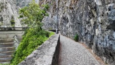 Matka Kanyonu 'nun yapay gölünün etrafındaki beton duvar, su yüzeyinde yüzen yapraklar ve molozlar ve üzerinde metal bir patika var.
