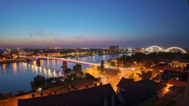 Novi Sad 'ın Tuna Nehri ve Petrovaradin kalesi üzerindeki aydınlık Varadin köprüsünün Sırbistan' da büyüleyici bir kent manzarası yaratmasıyla, gün batımında, Time-LAPSE of Novi Sad 'ın renkli şehir manzarası