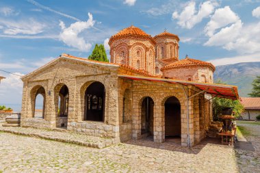 Kuzey Makedonya 'daki Aziz Naum manastırının manzarasında bir kilise, kaldırım taşı avlusu ve parlak mavi gökyüzü altında geleneksel mimari yer alıyor.