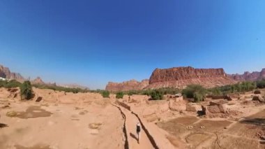 El-Ula, Suudi Arabistan 'daki kızıl kumtaşı dağlarının eteklerindeki vaha ve eski şehrin kalıntılarından geçen eski çiftliklerde yürüyen bir turist.