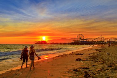 Santa Monica, Kaliforniya, ABD - 8 Ağustos 2018: Santa Monica İskelesi, Pasifik Sahili 'nde gün batımında yürüyen kadın çift. Eğlence parkı, dönme dolap ve lunapark treni.