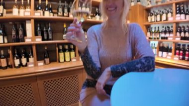 Zarif şapkası ve hayvan desenli kolları olan sarışın şarap garsonu İtalya 'da bir şarap mahzeninde beyaz şarap tadıyor, boyalı duvarlarıyla ünlü Emilia Romagna' da