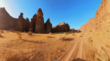 Suudi Arabistan 'ın çarpıcı çölünde macera ruhunu yakalayan, Alula Sharaan Doğa Koruma Alanındaki yüksek kumtaşı oluşumları boyunca toprak bir yolda ilerleyen off road aracı. Hava görünümü