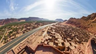 Alula Kalesi 'nin eski harabeleri ve Alula Eski Kasabası' ndaki modern yerleşimlere hükmeden nefes kesici hava manzarası çarpıcı bir çöl manzarasına karşı.