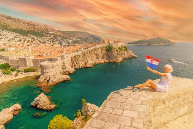 Hırvatistan 'ın Dubrovnik surlarına bakan Lovrijenac Kalesi' nde Hırvat bayrağı taşıyan bir kadın. Dalmaçya 'da Hırvatistan' ın Bokar Kalesi ile Dubrovnik 'in Batı Limanı' nda gün batımı. UNESCO duvarlı kasaba.