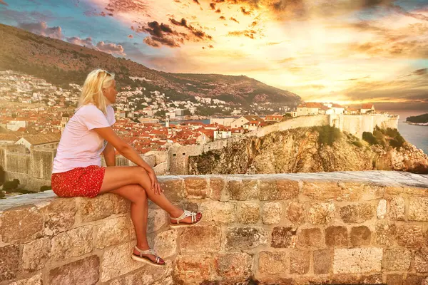Batı limanında gün batımında Lovrijenac kalesinde dinlenen bir kadın. Hırvatistan 'daki Bokar Kalesi ile Dubrovnik şehir manzarası. Dalmaçya 'nın tarihi kenti ve UNESCO Dünya Mirası Alanı.