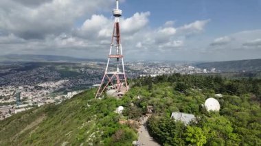 Dönme dolap kulübesinden TV kulesi manzarası Tiflis şehir manzarasına ve Georgia 'da bulutlu bir gökyüzünün altındaki çevreye doğru ilerliyor.