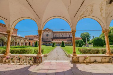 Ferrara, İtalya - 17 Mayıs 2025: İtalya 'nın Ferrara şehrinde güneşli bir yaz gününde manastır kemerleriyle, yeşil çimlerle, çalılarla ve mavi gökyüzüyle çevrili Aziz Christopher Kilisesi