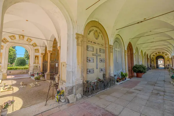 Ferrara, İtalya - 17 Mayıs 2025: Ferrara mezarlığındaki kapalı bir geçitin duvarlarını kaplayan dua eden kadın heykelleri ve mermer mezarlar karmaşık ayrıntılar ve mezar taşları
