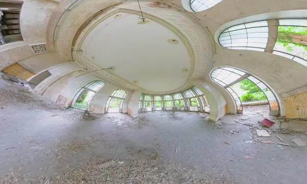 Gürcistan 'ın Tskaltubo kentindeki çürüyen Sanatoryum Metalürjistinin panoramik görüntüsünde, kemerli pencereler, enkaz saçılmış yerler ve büyük bir iç mekanın kalıntıları yer alıyor.