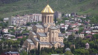 Gürcistan 'ın başkenti Tiflis' te güneşli bir günde muhteşem altın kubbesine sahip olan Sameba Katedrali veya Kutsal Üçlü Katedrali, meskun binalar ve yemyeşil ağaçlar arasında görkemli bir şekilde yükseliyor.