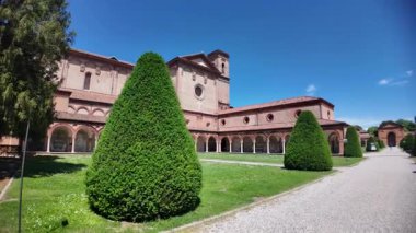 Güneşli bir günde manastırı ve cephesi olan Ferrara 'daki Aziz Christopher Kilisesi, manikürlü çimenler ve koni biçimli çalılarla çevrilidir.