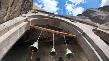 Vardzia, Gürcistan, 1 Mayıs 2025: Vardzia 'daki Dormition Kilisesi girişinde çanlar antik freskleri ve manzaralı gökyüzünü vurguluyor.