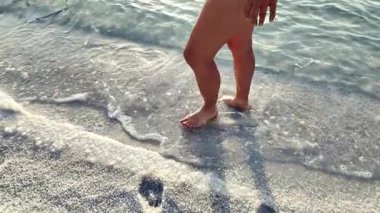 Ürdün 'de tuzla kaplı eşsiz bir plajda yürüyen yalın ayak bir birey sahil boyunca ayak izleri bırakıyor ve dalgalar yavaşça içeri dalıyor.