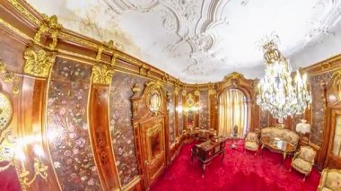 Transilvanya, Romanya - 25 Ağustos 2025: Zengin ahşap paneller, altın süslemeler, çiçek desenleri ve büyük bir kristal avize sergilenen Peles Kalesi İçişleri Odası