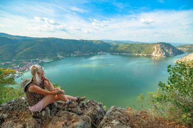 Kayaların üzerinde oturan kadın, Romanya 'daki Tuna Nehri vadisinin geniş panoramik manzarasının keyfini çıkarıyor ve Sırbistan ve Romanya sınırındaki Cerdap Ulusal Parkı' ndaki orman dağlarının tadını çıkarıyor.