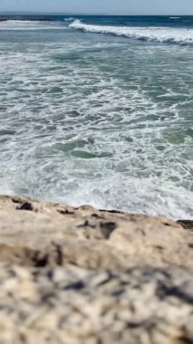 Huzurlu bir görüntü, geniş kumlu bir plajda, açık gökyüzü ve arka planda hafif dalgalar olan iki insanı, sakin bir şekilde yürürken gösteriyor..