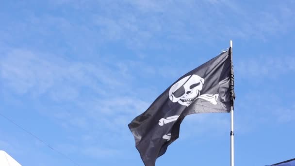 青い空に向かって風になびくジョリー ロジャー海賊旗 白い頭蓋骨と十字架のついた黒い海賊旗 閉めろ スローモーション 高品質のフルHd映像 — ストック動画