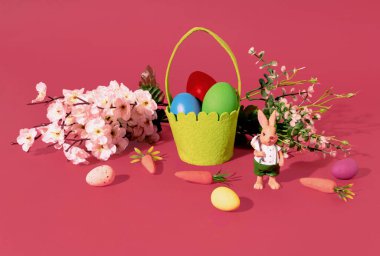 Easter Bunny, eggs in basket, carrots spring tree branch and flowers on red background. Minimal horizontal composition, Easter decoration concept
