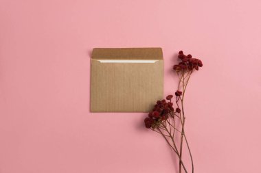 Mockup of an open card made of kraft paper with dried red flowers on a pink background