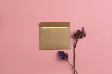 Mockup of an open card made of kraft paper with dried blue flowers on a pink background