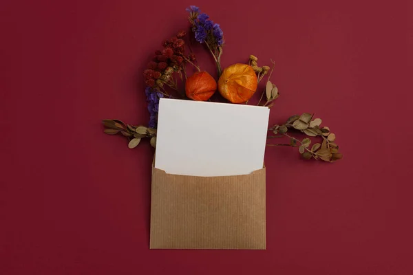 Composition of Dried Flowers on Craft Envelope Letter Mockup with Blank White Paper on Red Background