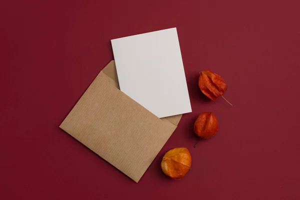Mockup of an Open Blank Letter and Envelope with Dried Physalis Flowers on Burgundy Background