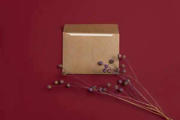 A kraft postal letter is adorned with a charming composition of dried flowers, including both dry and painted flax flowers, set against a striking red background. The delicate blooms add a touch of natural beauty and rustic elegance to the letter's a