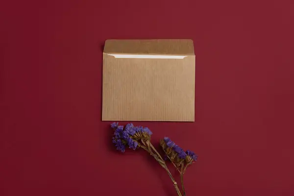 Mockup of an open letter made of kraft paper, set against a rich burgundy background, and adorned with beautiful blue dried flowers