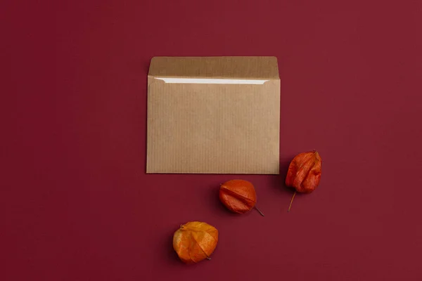Mockup of an open envelope decorated with dried orange physalis flowers on a burgundy background