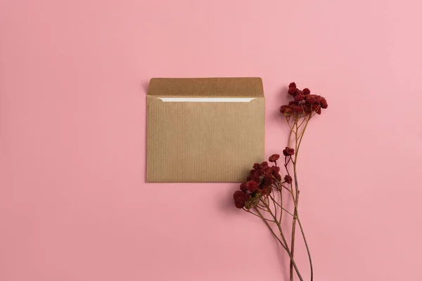 Mockup of an open card made of kraft paper with dried red flowers on a pink background