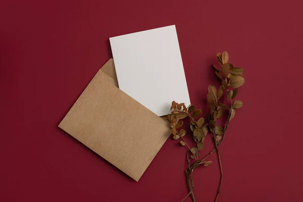 Mockup ?raft postal letter decorated with a composition of dried flowers, including dry blueberry leaves on red background