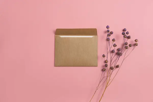 Mockup of an open card made of craft paper with a composition of dyed flax flowers on a pink background