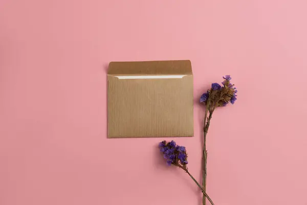 Mockup of an open card made of kraft paper with dried blue flowers on a pink background