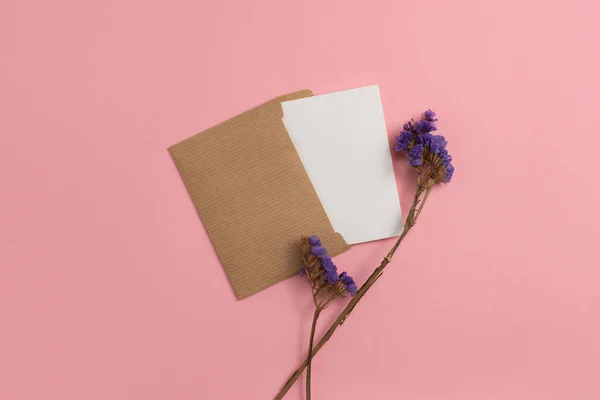 An open greeting card made from environmentally friendly materials and adorned with dried blue flowers on a pink background