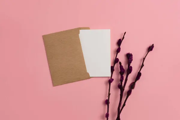 An open card made from eco-friendly materials and decorated with dried flowering and dyed in red color branches on a pink background