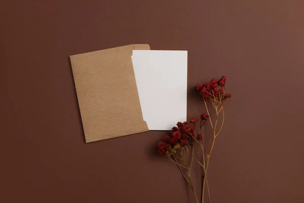 Mockup of a card made from eco-friendly materials and decorated with a composition of dried flowers dyed in red color and placed on a brown background