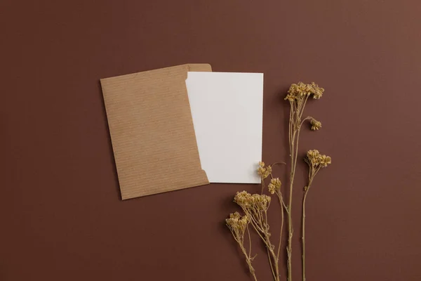 Mockup of a card made from eco-friendly materials and decorated with a composition of dried flowers placed on a brown background